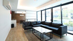 A modern living room with a black leather sofa, a white coffee table, and a large window offering a view of the outside. - 1 Bedroom Adelaide CBD Centre Apartment (Adelaide)