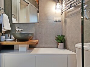 A modern bathroom with a large vessel sink, a mirror, a small potted plant, and a towel rack.