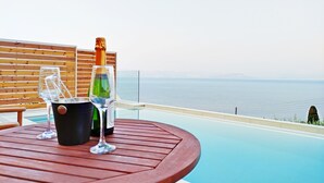 Ein Holztisch mit einer Champagnerflasche und zwei Gläsern, mit Blick auf einen Pool und das Meer.