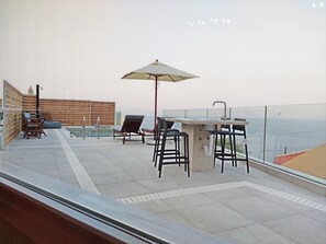 A rooftop terrace with a bar area, lounge chairs, and a view of the sea.