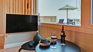 Ein modernes Wohnzimmer mit Fernseher, einem Tisch mit Trauben und Weingläsern sowie Blick auf einen Balkon mit Gartenmöbeln.