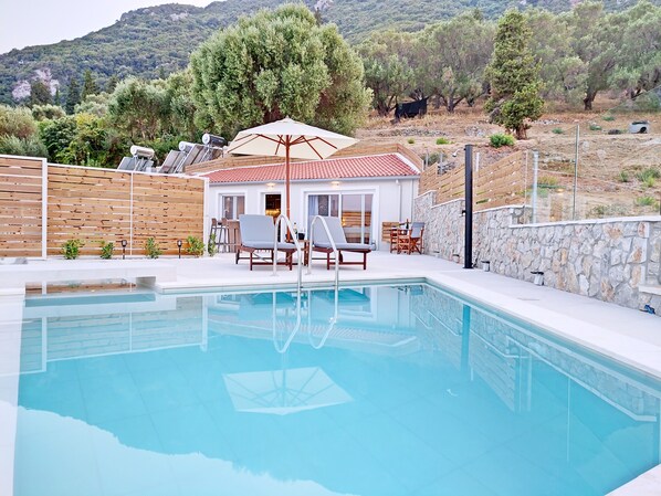 A swimming pool with lounge chairs and a table, surrounded by a wooden fence and a stone wall.