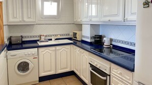 Una cocina con armarios blancos, lavadora, microondas y cafetera.