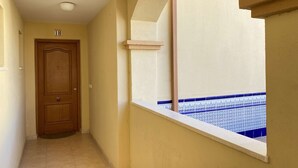 Un pasillo con una puerta de madera, una ventana con azulejos azules estampados y una pared color beige.