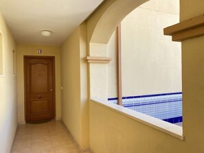 A hallway with a wooden door, a window with blue patterned tiles, and a beige wall.