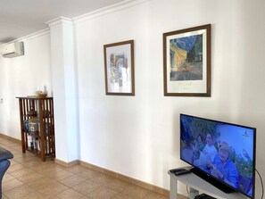 Un salon avec un téléviseur, des œuvres d’art encadrées et une bibliothèque.