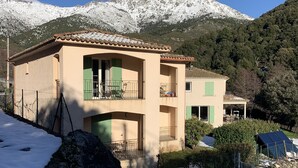A two-story building with a balcony, set against a backdrop of snow-covered mountains. - NICE APARTMENT IN HAMLET 700 M / north pond, fiber, solar hot water (Santa-Lucia-Di-Mercurio)