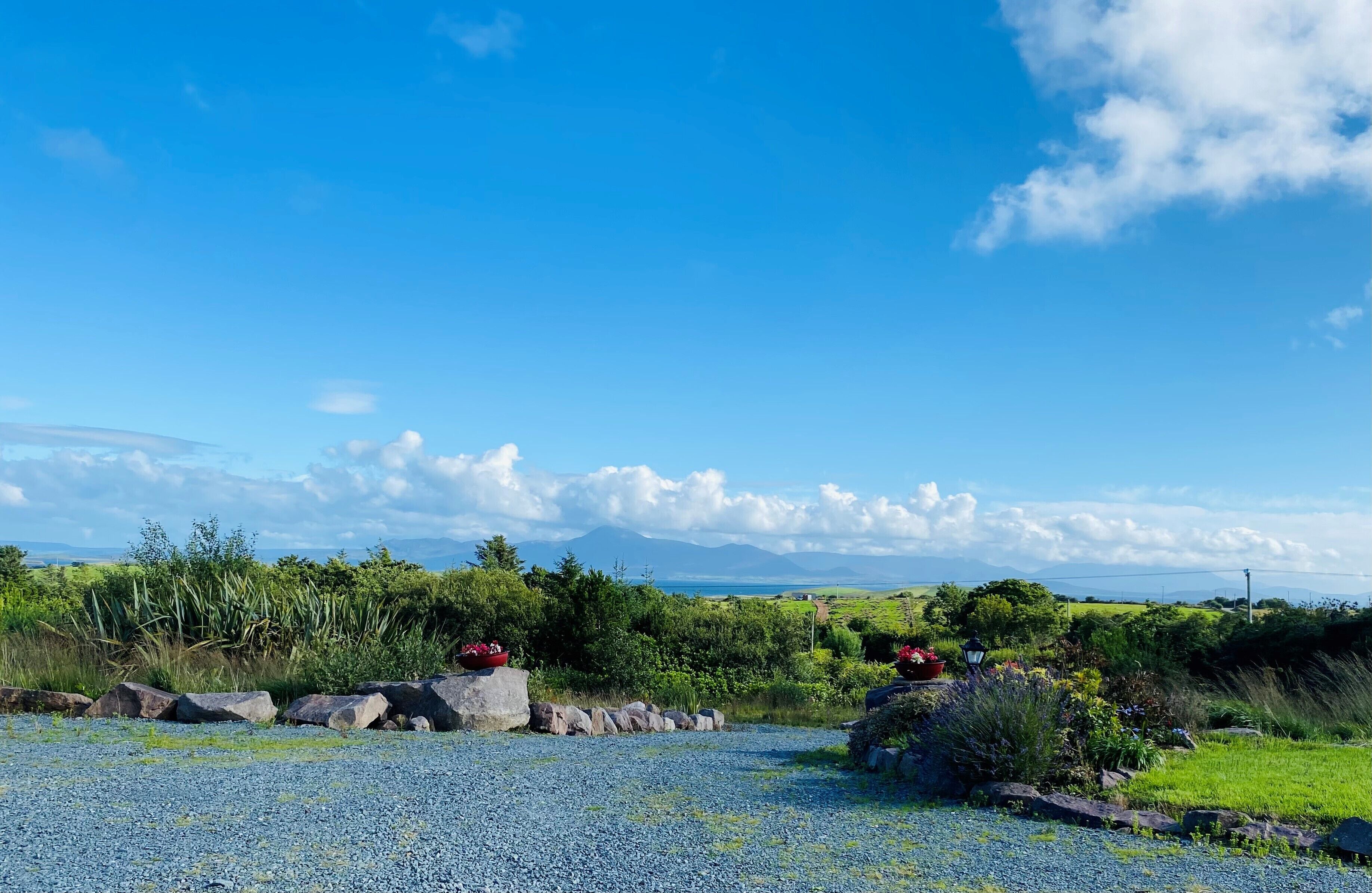 A gravel path leading to a garden with a view of distant mountains.
