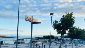Eine Uferpromenade mit Bänken, einem Wegweiser und einer Laterne.