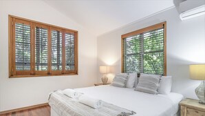 Ein Schlafzimmer mit einem großen Bett, zwei Fenstern mit Holzrahmen, einer Nachttischlampe und einem Nachttisch.