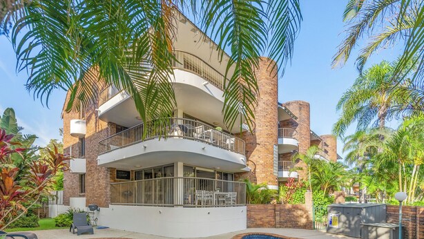 Un edificio moderno con piscina, rodeado de exuberante vegetación y palmeras.