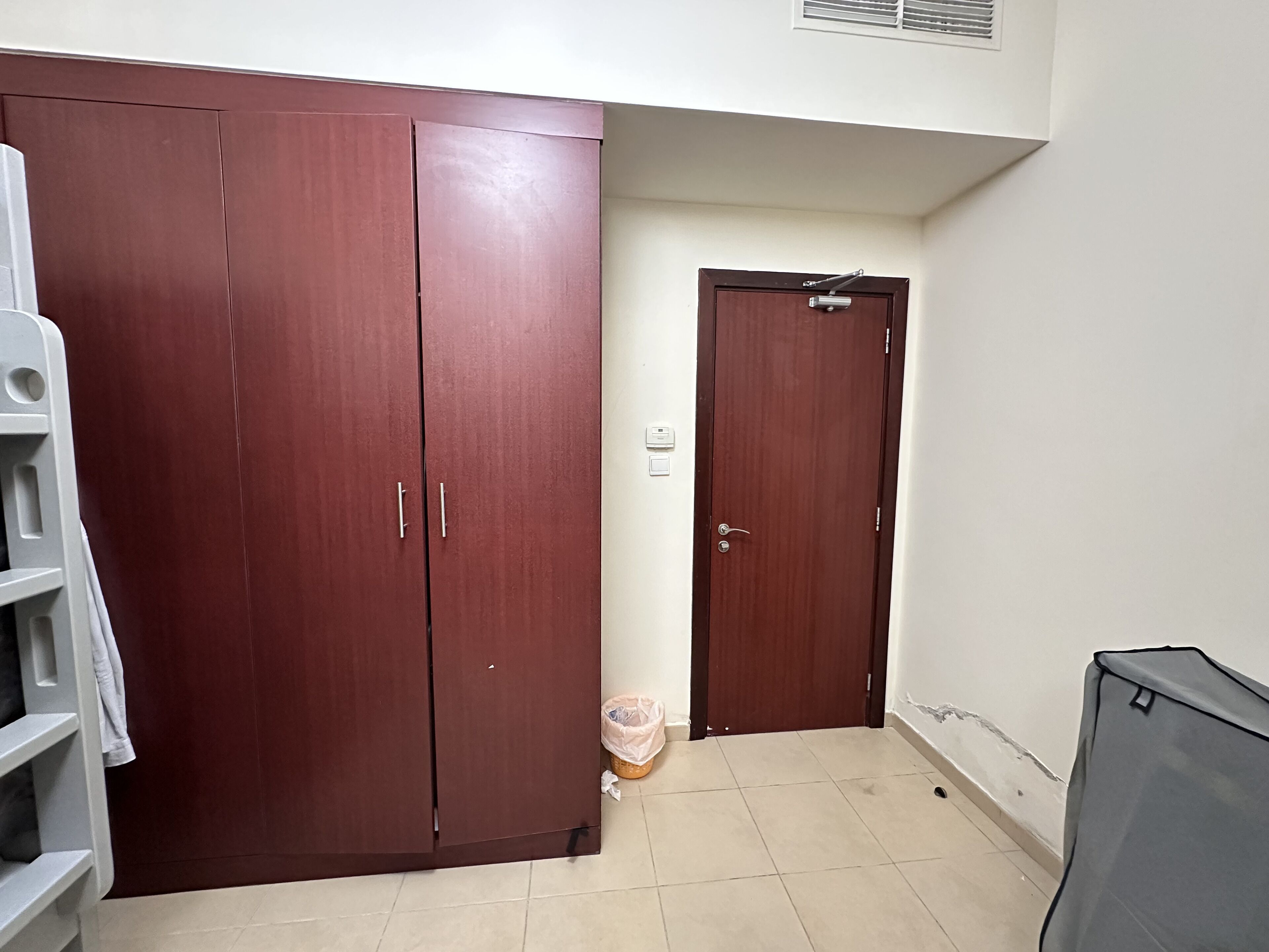 A room with a large wardrobe, a door, and a tiled floor.