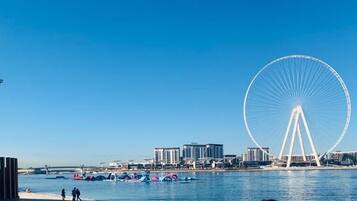 A waterfront cityscape with a large Ferris wheel, modern buildings, and a clear blue sky.