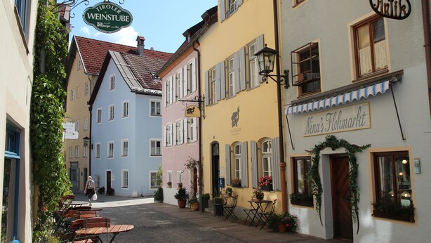 A narrow street with colorful buildings, outdoor seating, and signs for local businesses. - Cozy vacation apartment, (Füssen)