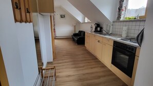 A modern kitchen with wooden cabinets, a black oven, and a window with curtains. - Cozy vacation apartment, (Füssen)