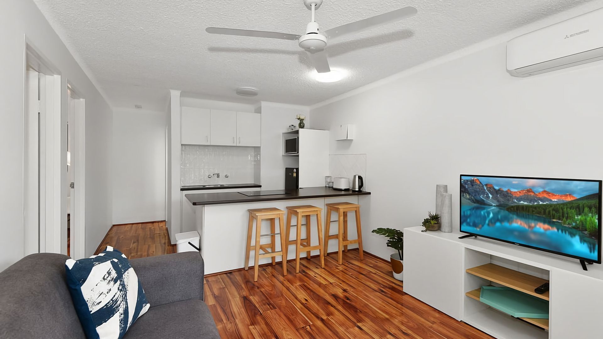 A modern kitchen with a bar area, a dining table, and a TV on a stand.