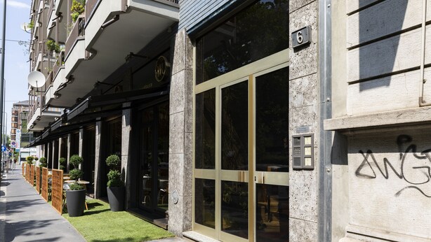 A building with large glass doors, a stone facade, and a small grassy area with potted plants.