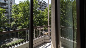 A balcony with a view of a multi-story building, trees, and a street.