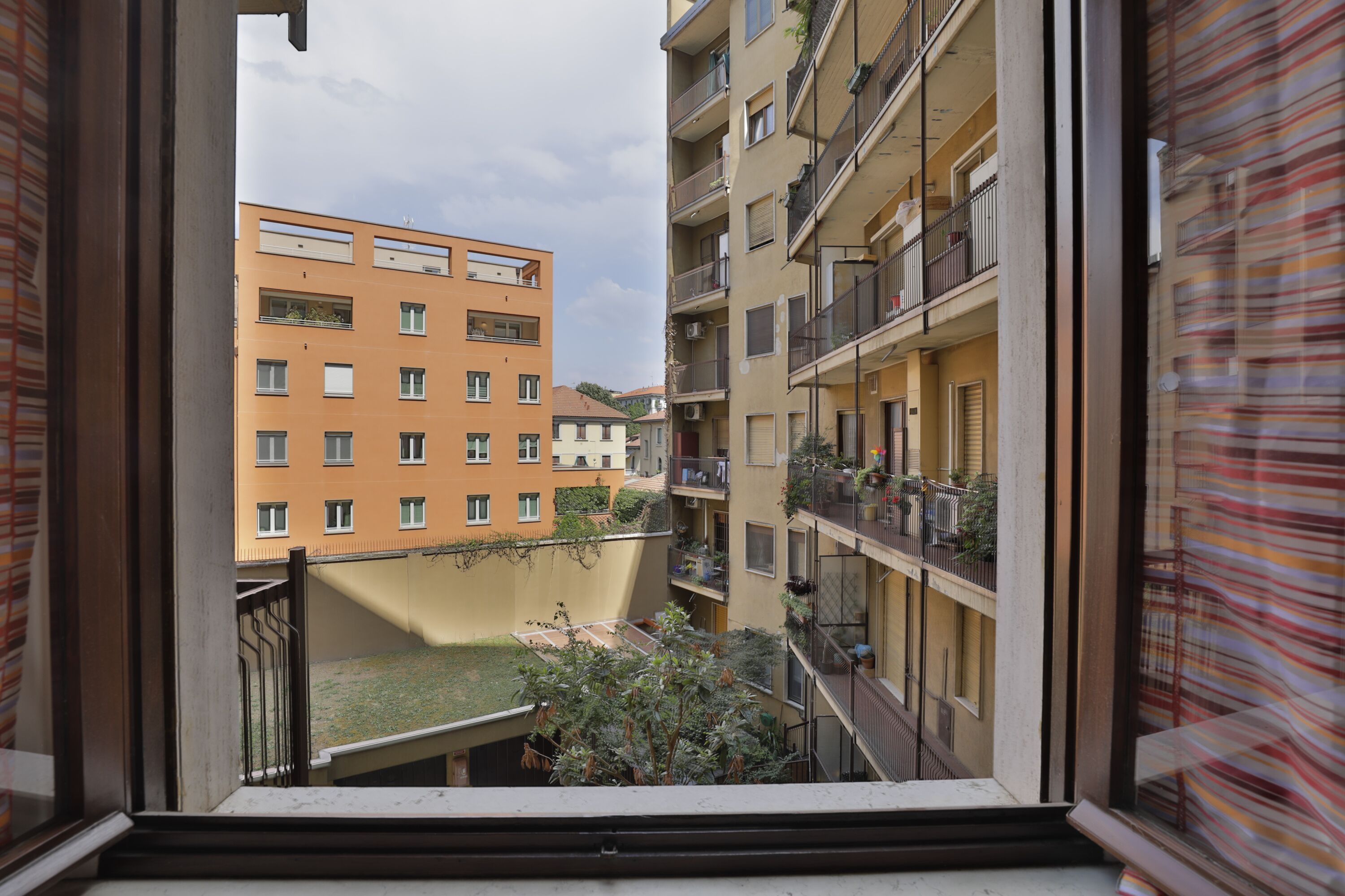 A view from a window overlooking a courtyard with a building featuring balconies and a flat roof.