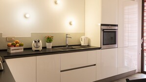 A modern kitchen with white cabinets, a black countertop, a built-in oven, a kettle, and a fruit bowl.