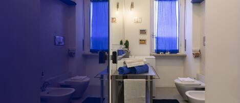 A modern bathroom with a bidet, toilet, and sink. There are towels on the counter and a black bath mat on the floor.