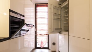 A modern kitchen with white cabinetry, a built-in oven, and a glass door with a striped pattern.