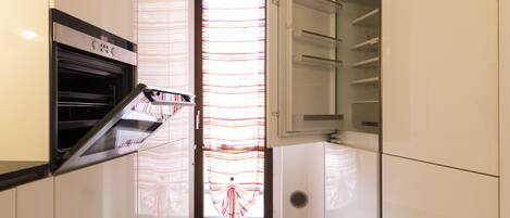 A modern kitchen with white cabinetry, a built-in oven, and a glass door with a striped pattern.