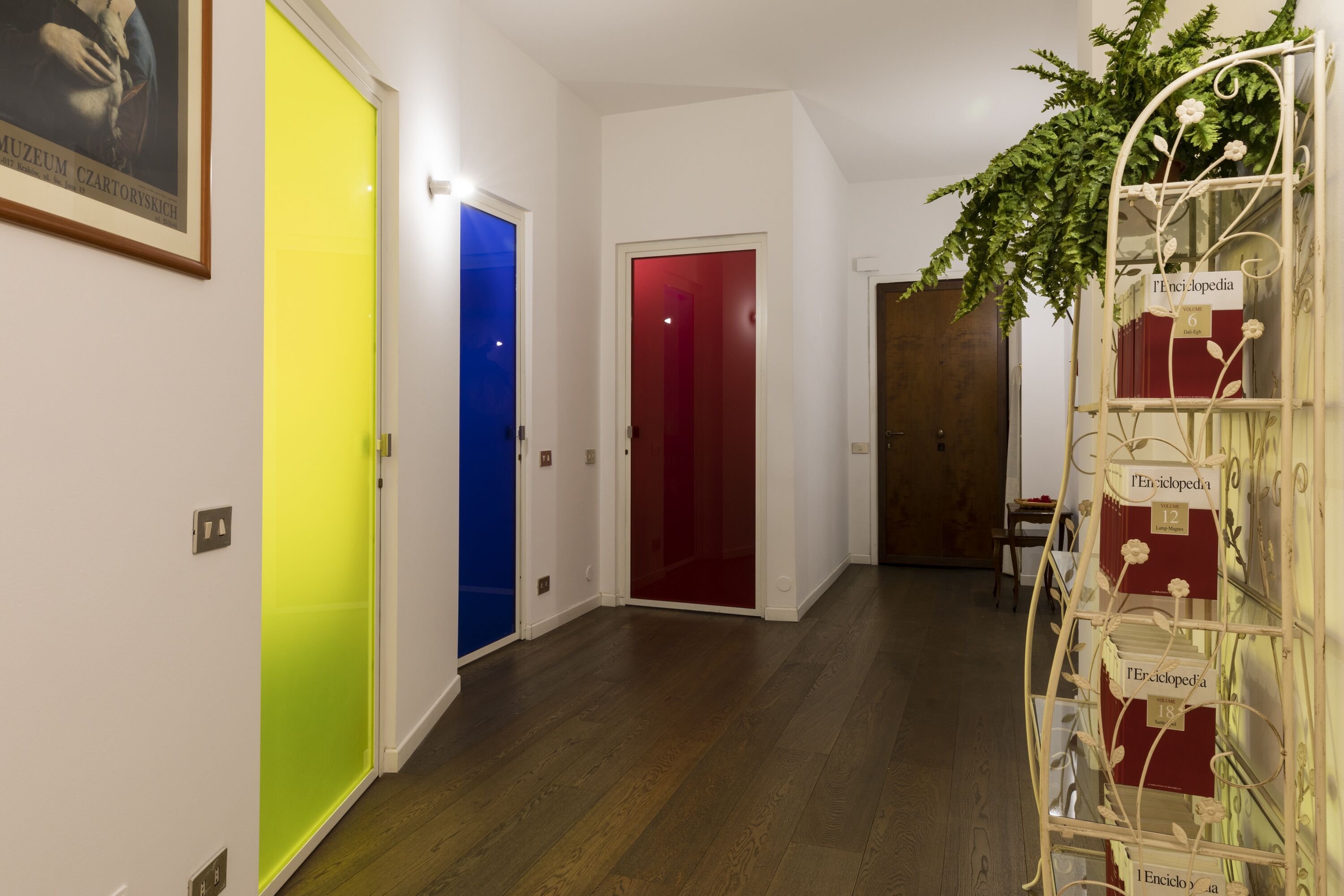 A hallway with a wooden floor, a metal plant stand, and a framed picture on the wall.