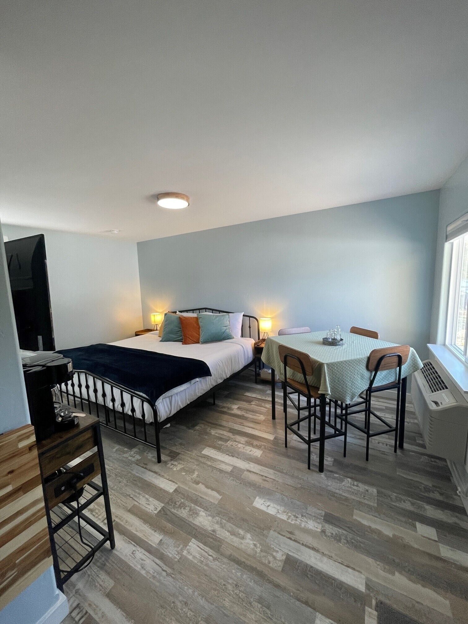A compact room with a bed, bedside table, and a small desk with a chair.