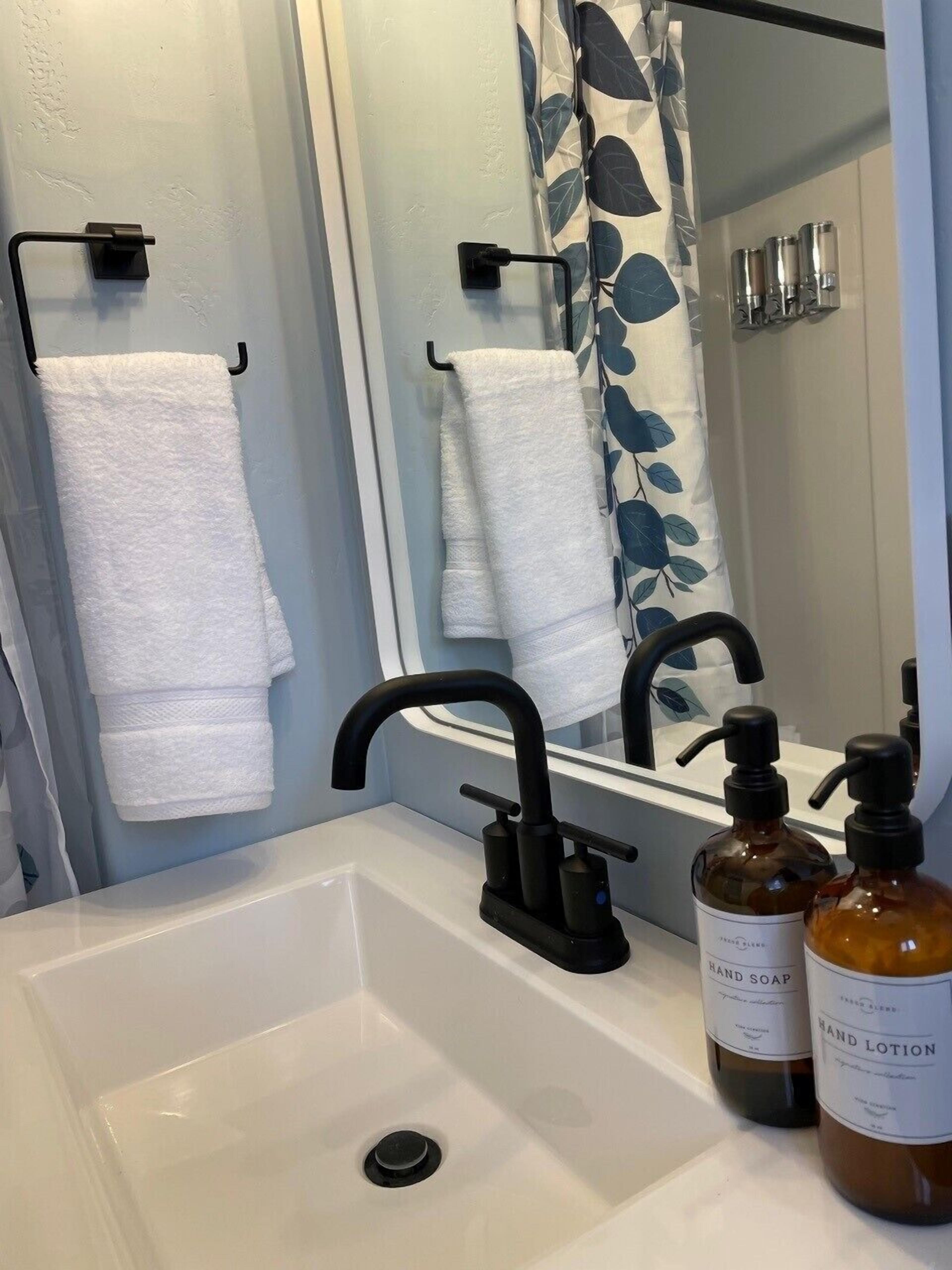 Une salle de bain avec un lavabo blanc, un robinet noir et deux flacons de savon liquide et de lotion pour les mains.