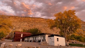 Un bâtiment rustique à l’extérieur rouge et aux murs blancs, avec une allée en gravier et un grand arbre à l’avant.