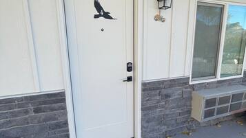Une porte blanche ornée d’un motif d’oiseau, un paillasson et un mur en pierre.