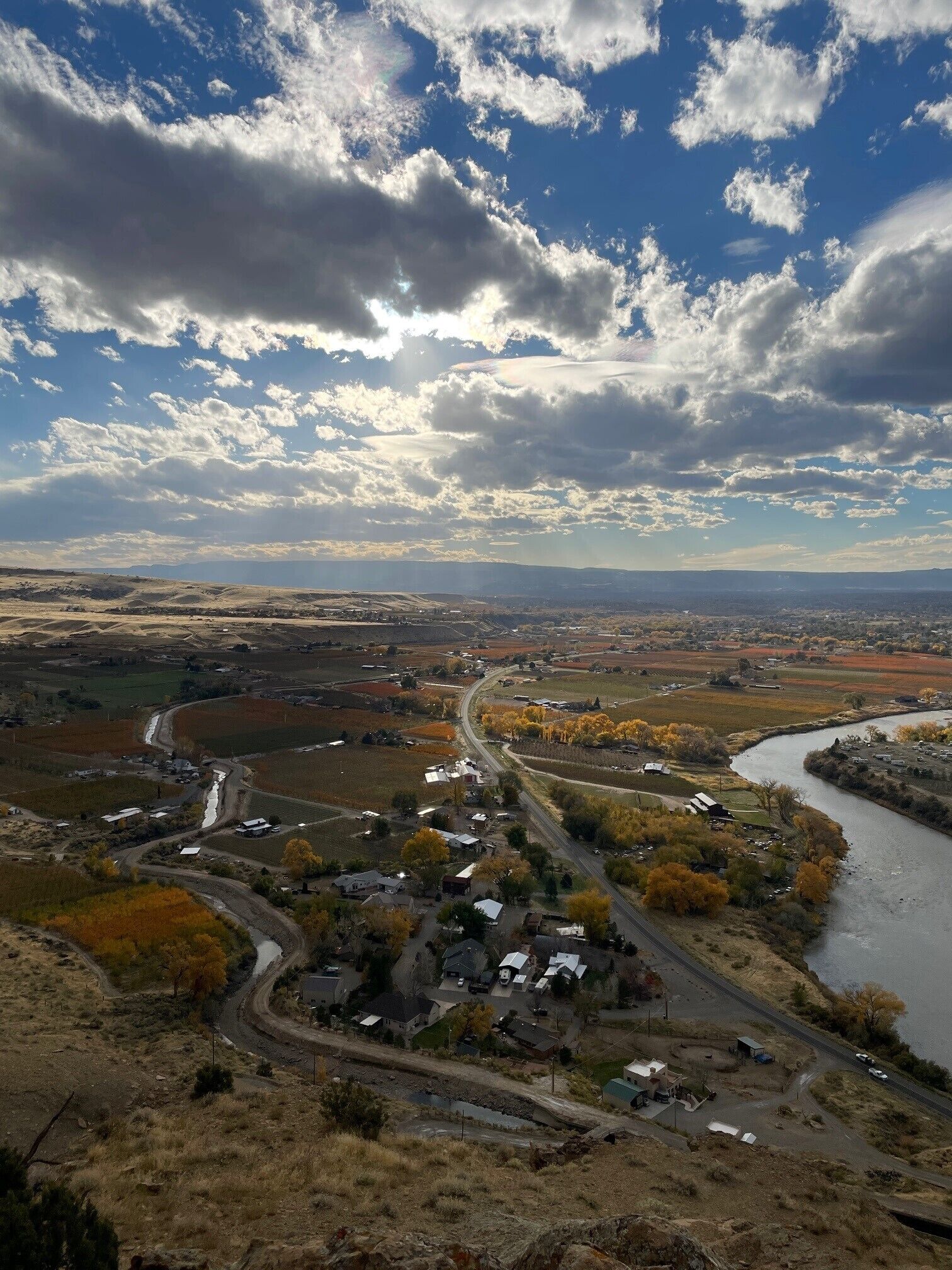 A rural landscape with a winding river, a small settlement, and a clear sky.