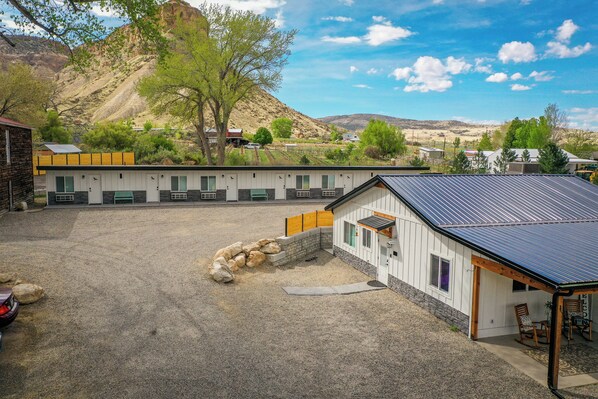 A motel with a gravel parking area, a covered outdoor seating area, and a mountainous backdrop.