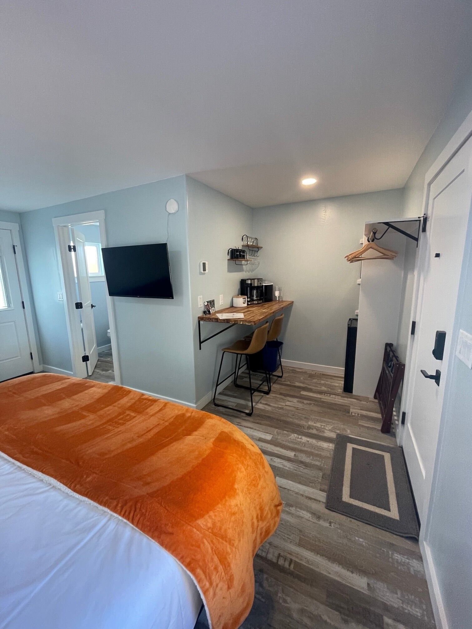 A hotel room with a bed, a desk with a chair, a coffee maker, and a TV mounted on the wall.