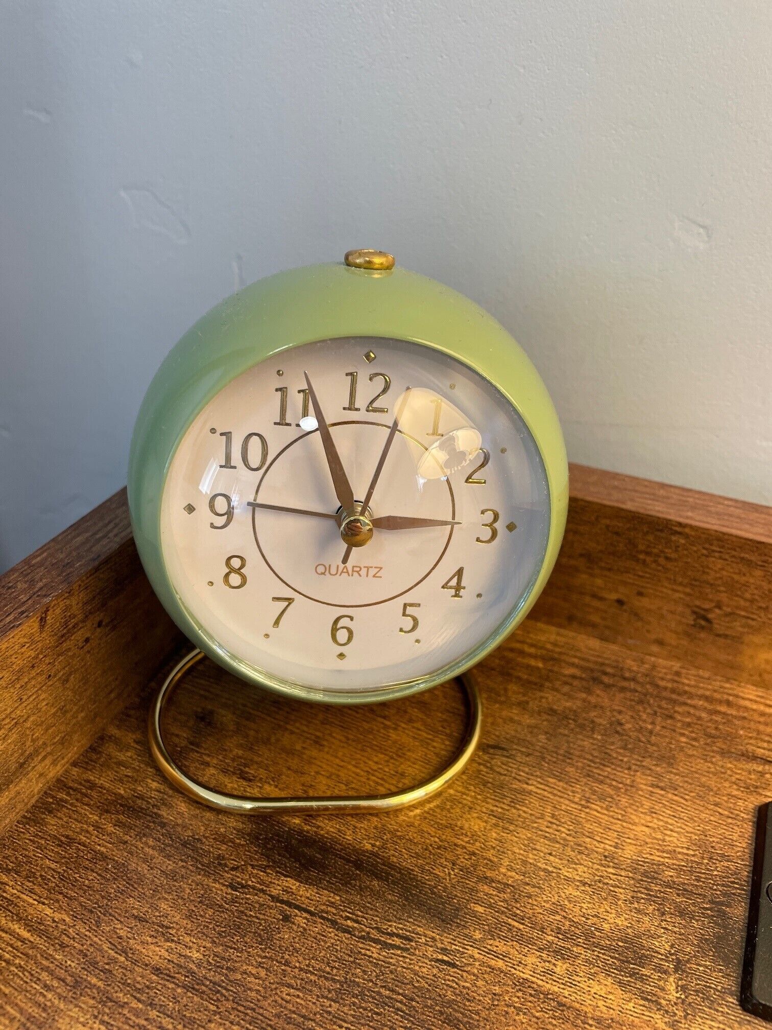 Een groen kwarts wekkerradio met een witte wijzerplaat en gouden cijfers, op een houten ondergrond.