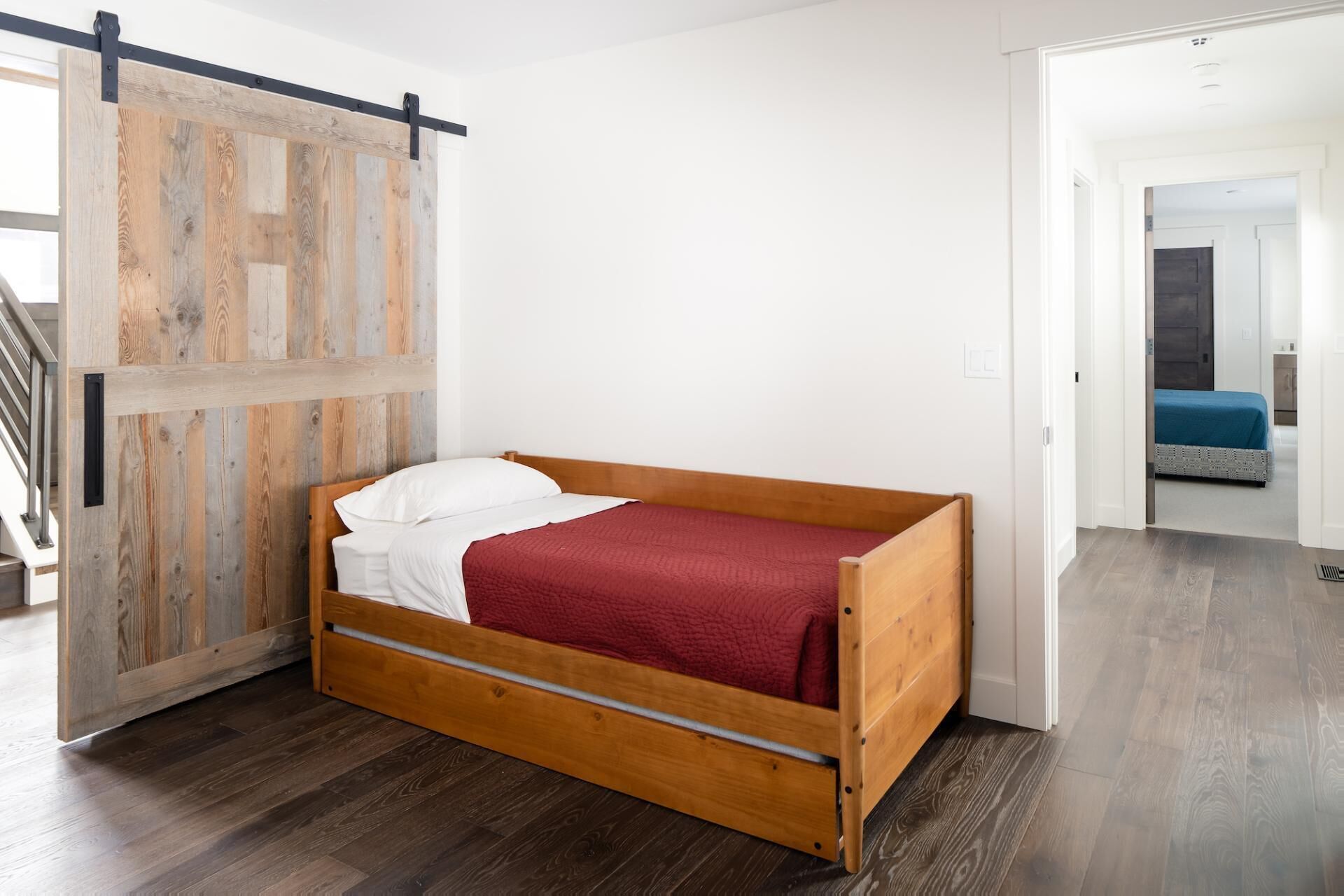 A single wooden bed with a red blanket in a room with wooden flooring and a sliding barn door.