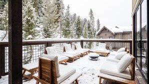 Terraza de madera con mobiliario exterior y vista a árboles nevados.