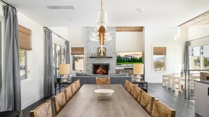 Un comedor amplio con una larga mesa de madera y sillas tejidas, una chimenea y una pantalla de televisión grande.