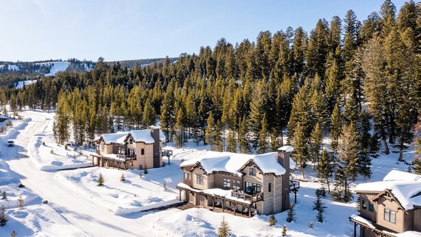 Un alojamiento cubierto de nieve con varias cabañas, rodeado de un bosque frondoso y un cielo despejado.