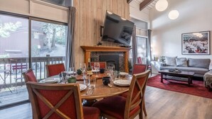A dining area with a wooden table set for four, a fireplace, and a television above it. - Townhome on the Ski Back Trail! Fireplace! Shared Amenities! (Mammoth Lakes)