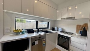 Una cocina moderna con armarios blancos, lavavajillas integrado, estufa a gas y un ventanal que proporciona luz natural.