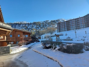 Uma cabana de madeira com varanda, uma parede de pedra e um caminho coberto de neve que leva a uma montanha.