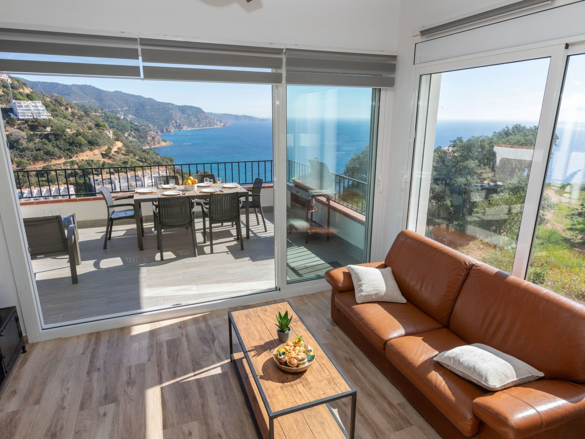 A modern living room with a large sliding glass door leading to a balcony with a scenic ocean view.