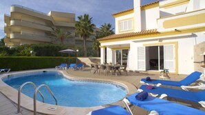 A swimming pool with lounge chairs, a table, and a building with balconies. - Vacation home Inês by Interhome (Gale)