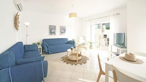 A modern living room with a blue sofa set, a round coffee table, and a dining area with a white table and chairs. - Vacation home Inês by Interhome (Gale)