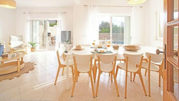 A bright, spacious dining area with a round table, white chairs, and a television. - Vacation home Inês by Interhome (Gale)
