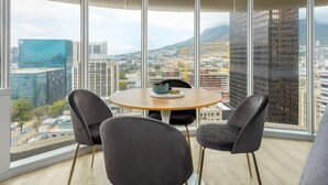 Ein modernes Zimmer mit einem runden Tisch, zwei Stühlen und großen Fenstern mit Blick auf die Stadt.