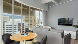 Ein modernes Wohnzimmer mit grauem Sofa, schwarzen Sesseln, einem Holztisch und einem Fernseher an der Wand.