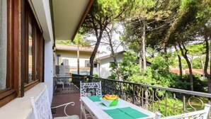 A balcony with a table and chairs, surrounded by trees and a building in the background.
